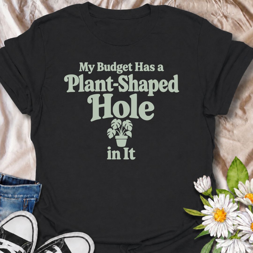 A funny plant T-shirt for anyone whose budget seems to disappear every time a new houseplant comes into view. The phrase “My Budget Has a Plant-Shaped Hole in It” delivers dry, self-aware humor that plant parents and collectors will instantly relate to. Featuring bold retro typography with a small potted plant accent, the design stays clean, readable, and easy to wear. It makes a great gift for nursery regulars, houseplant lovers, and anyone who keeps spending their spare cash on one more plant. Perfect for