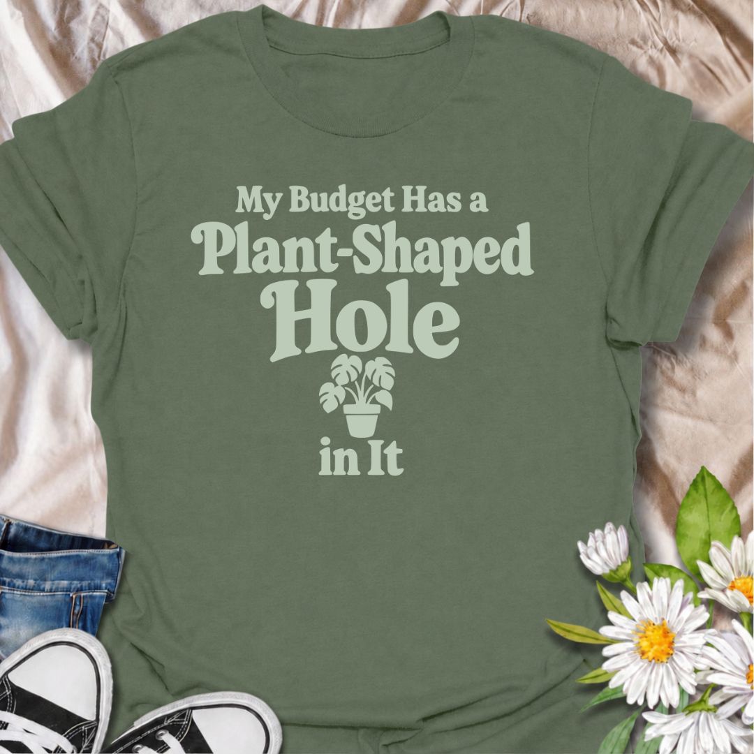 A funny plant T-shirt for anyone whose budget seems to disappear every time a new houseplant comes into view. The phrase “My Budget Has a Plant-Shaped Hole in It” delivers dry, self-aware humor that plant parents and collectors will instantly relate to. Featuring bold retro typography with a small potted plant accent, the design stays clean, readable, and easy to wear. It makes a great gift for nursery regulars, houseplant lovers, and anyone who keeps spending their spare cash on one more plant. Perfect for