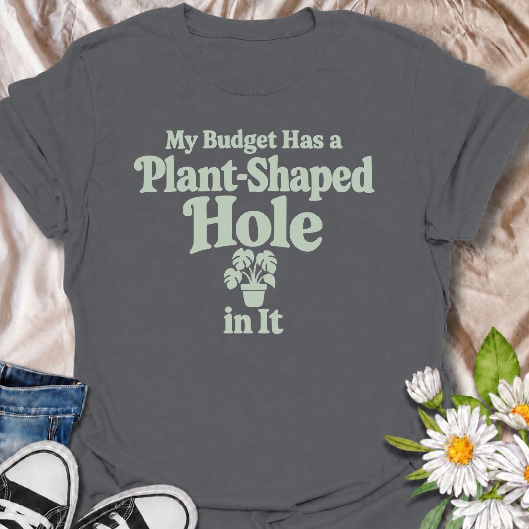 A funny plant T-shirt for anyone whose budget seems to disappear every time a new houseplant comes into view. The phrase “My Budget Has a Plant-Shaped Hole in It” delivers dry, self-aware humor that plant parents and collectors will instantly relate to. Featuring bold retro typography with a small potted plant accent, the design stays clean, readable, and easy to wear. It makes a great gift for nursery regulars, houseplant lovers, and anyone who keeps spending their spare cash on one more plant. Perfect for