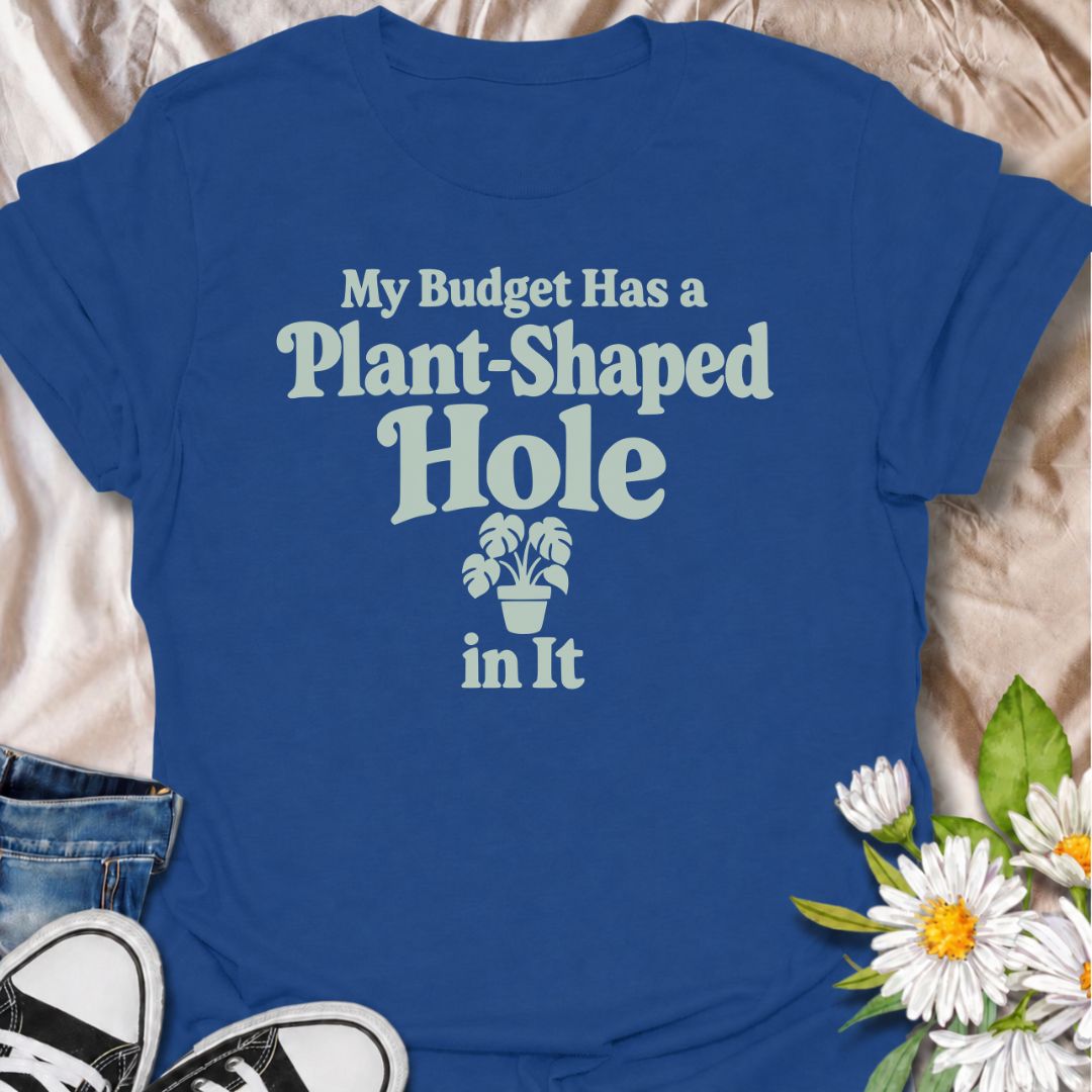 A funny plant T-shirt for anyone whose budget seems to disappear every time a new houseplant comes into view. The phrase “My Budget Has a Plant-Shaped Hole in It” delivers dry, self-aware humor that plant parents and collectors will instantly relate to. Featuring bold retro typography with a small potted plant accent, the design stays clean, readable, and easy to wear. It makes a great gift for nursery regulars, houseplant lovers, and anyone who keeps spending their spare cash on one more plant. Perfect for