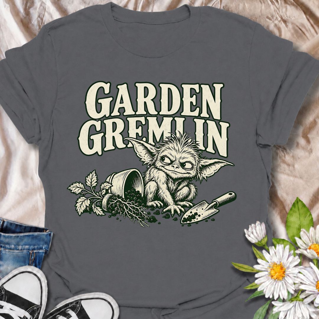 A funny gardening T-shirt for anyone who turns a simple garden job into a slightly chaotic adventure. Featuring a mischievous little garden gremlin beside spilled soil, a tipped plant pot, and a hand trowel, this design is packed with personality and relatable garden humor. The bold “Garden Gremlin” phrase makes it perfect for backyard gardeners, plant lovers, and anyone who is rarely clean or organized once gardening starts. It makes a fun gift for gardeners who embrace the mess, the dirt, and the occasion