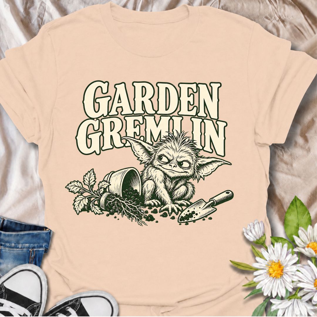 A funny gardening T-shirt for anyone who turns a simple garden job into a slightly chaotic adventure. Featuring a mischievous little garden gremlin beside spilled soil, a tipped plant pot, and a hand trowel, this design is packed with personality and relatable garden humor. The bold “Garden Gremlin” phrase makes it perfect for backyard gardeners, plant lovers, and anyone who is rarely clean or organized once gardening starts. It makes a fun gift for gardeners who embrace the mess, the dirt, and the occasion