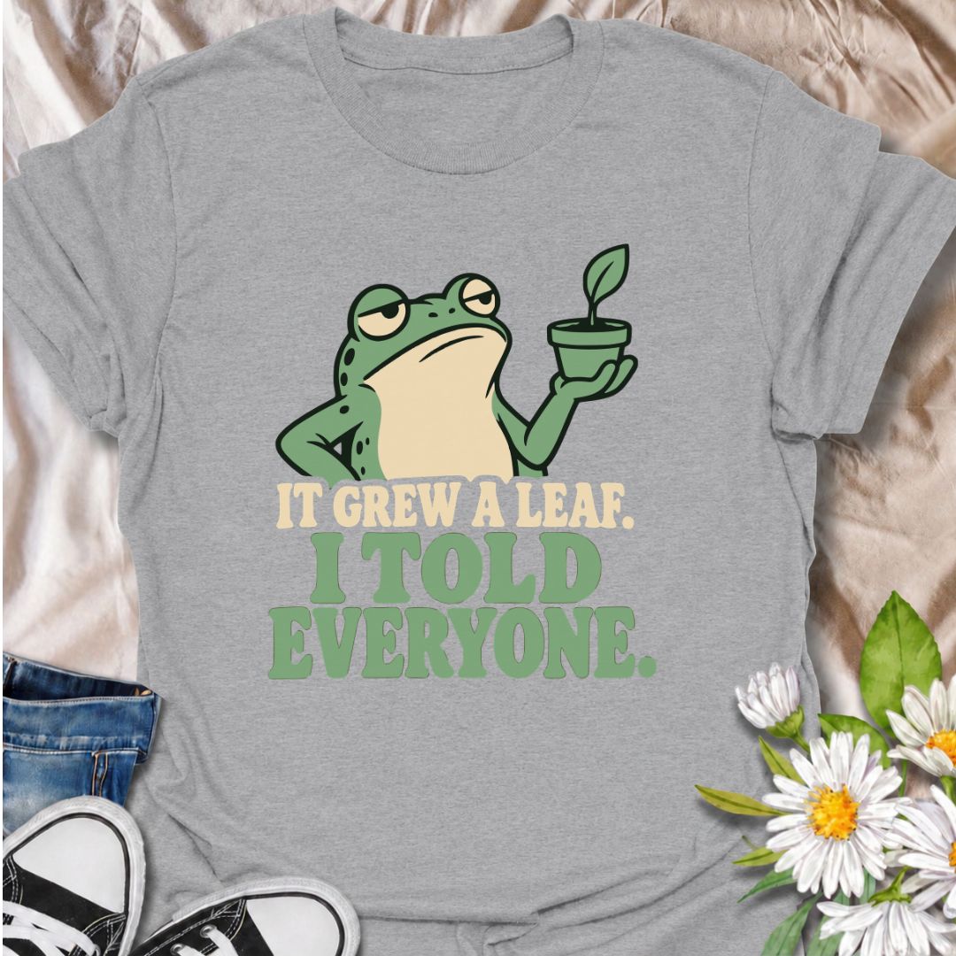 A funny plant T-shirt for anyone who celebrates every tiny bit of new growth like a major event. Featuring a deadpan frog proudly holding up a small plant, the phrase “It Grew a Leaf. I Told Everyone.” captures classic plant-parent behavior perfectly. It is ideal for houseplant lovers, indoor gardeners, propagation fans, and anyone who checks their plants for new growth far too often. The character-led design keeps the humor clear while giving it plenty of personality. A great gift for plant collectors, fro