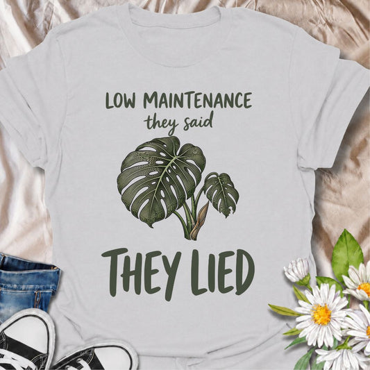 A funny plant T-shirt for anyone who was promised an easy-care houseplant and quickly discovered otherwise. The phrase “Low Maintenance, They Said. They Lied.” delivers dry, relatable humor that plant parents and monstera lovers will instantly understand. Featuring a leafy monstera illustration, the design feels simple, wearable, and clearly rooted in houseplant culture. It makes a great gift for indoor gardeners, plant collectors, and anyone who has spent far more time troubleshooting a supposedly easy pla
