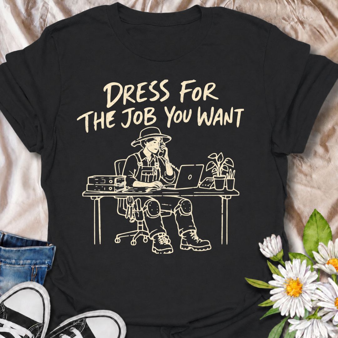 A funny gardening T-shirt for anyone who would rather be dressed for the garden than stuck behind a desk. The phrase “Dress for the Job You Want” pairs with a gardener in full work gear sitting in an office setting for a dry, absurd bit of garden humor. Featuring overalls, knee pads, work boots, tools, a laptop, and desk accessories, the design is perfect for gardeners who know exactly where they would rather be. It makes a great gift for professional gardeners, backyard growers, plant lovers, and anyone dr