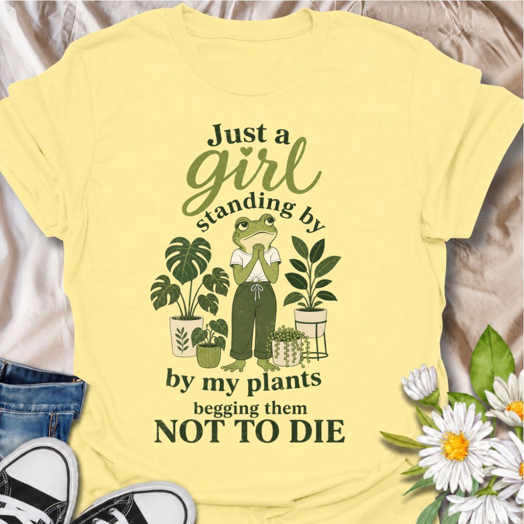 A funny plant T-shirt for anyone who spends far too much time encouraging their houseplants to stay alive. The phrase “Just a Girl Standing by My Plants Begging Them Not to Die” delivers relatable, self-deprecating humor for plant parents and indoor gardeners. Featuring a frog character surrounded by potted plants, the design feels playful, niche, and easy to wear. It makes a great gift for houseplant lovers, plant collectors, and anyone who has ever stared anxiously at a struggling leaf. Perfect for nurser