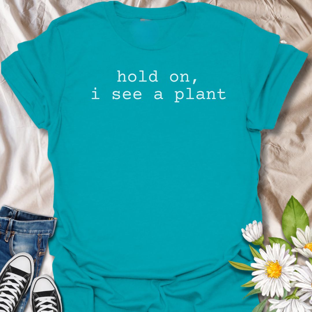 A funny plant T-shirt for anyone who gets instantly distracted the moment a houseplant comes into view. The phrase “Hold On, I See a Plant” captures that familiar plant-lover behavior with simple, dry humor. Its clean typewriter-style text keeps the design minimal, modern, and very easy to wear. It makes a great gift for plant parents, houseplant collectors, nursery regulars, and anyone whose attention is permanently drawn to greenery. Perfect for plant shopping, garden centers, casual weekends, or everyday