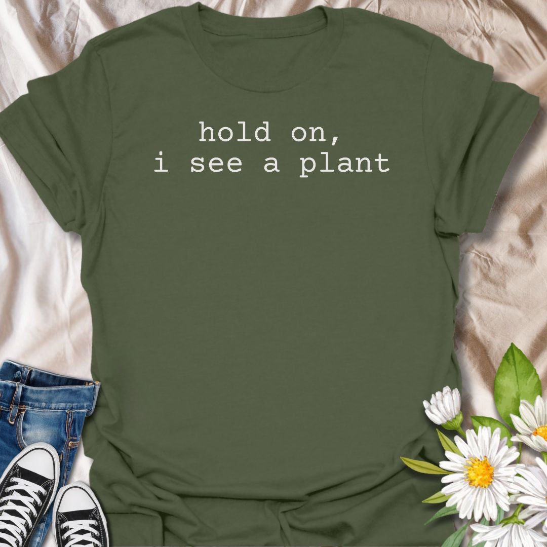 A funny plant T-shirt for anyone who gets instantly distracted the moment a houseplant comes into view. The phrase “Hold On, I See a Plant” captures that familiar plant-lover behavior with simple, dry humor. Its clean typewriter-style text keeps the design minimal, modern, and very easy to wear. It makes a great gift for plant parents, houseplant collectors, nursery regulars, and anyone whose attention is permanently drawn to greenery. Perfect for plant shopping, garden centers, casual weekends, or everyday