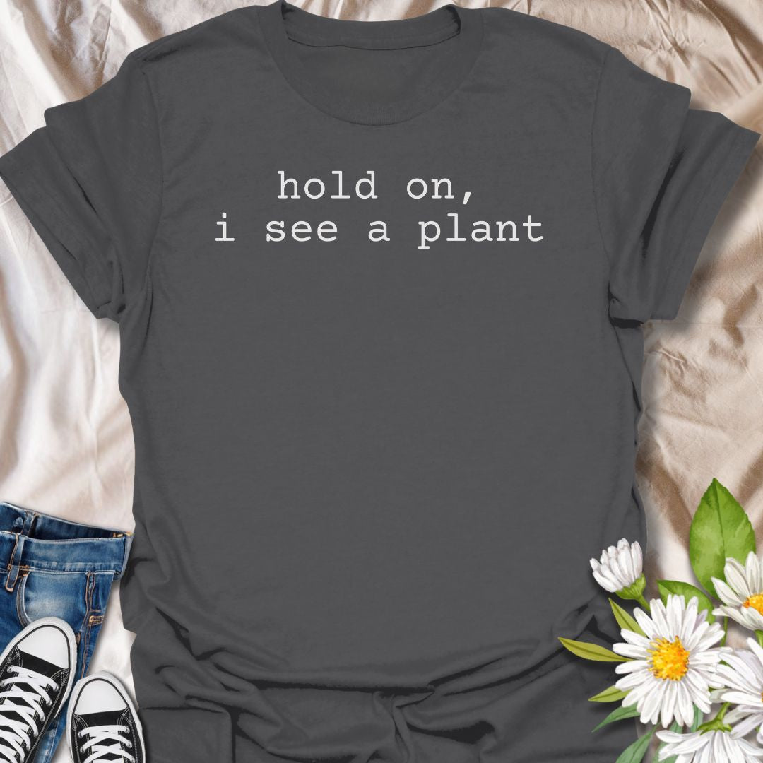A funny plant T-shirt for anyone who gets instantly distracted the moment a houseplant comes into view. The phrase “Hold On, I See a Plant” captures that familiar plant-lover behavior with simple, dry humor. Its clean typewriter-style text keeps the design minimal, modern, and very easy to wear. It makes a great gift for plant parents, houseplant collectors, nursery regulars, and anyone whose attention is permanently drawn to greenery. Perfect for plant shopping, garden centers, casual weekends, or everyday