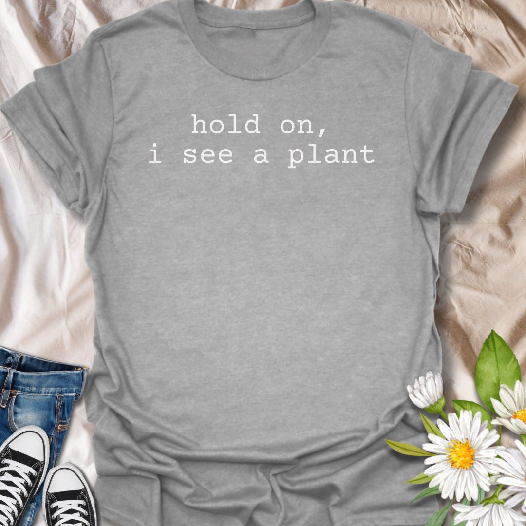 A funny plant T-shirt for anyone who gets instantly distracted the moment a houseplant comes into view. The phrase “Hold On, I See a Plant” captures that familiar plant-lover behavior with simple, dry humor. Its clean typewriter-style text keeps the design minimal, modern, and very easy to wear. It makes a great gift for plant parents, houseplant collectors, nursery regulars, and anyone whose attention is permanently drawn to greenery. Perfect for plant shopping, garden centers, casual weekends, or everyday