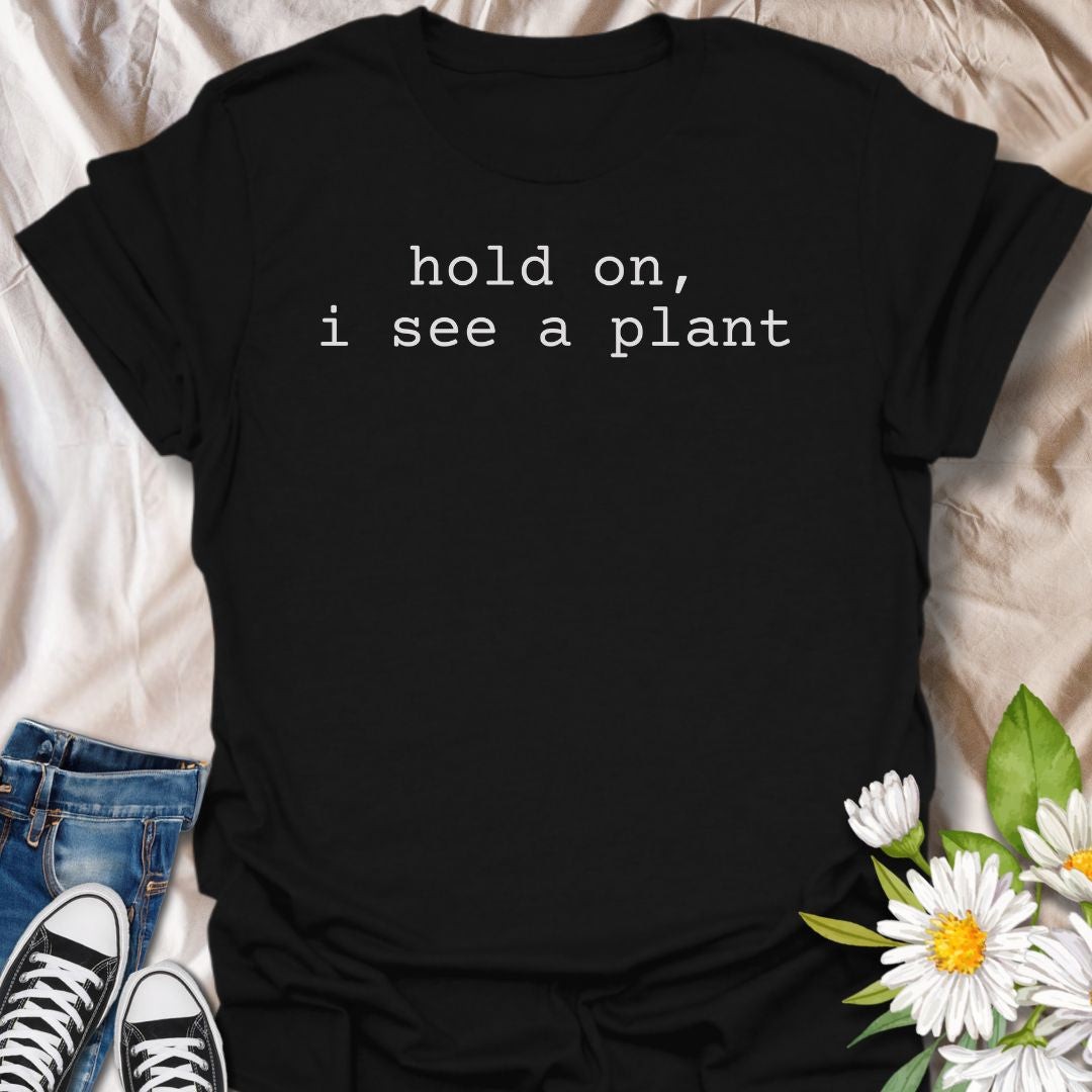 A funny plant T-shirt for anyone who gets instantly distracted the moment a houseplant comes into view. The phrase “Hold On, I See a Plant” captures that familiar plant-lover behavior with simple, dry humor. Its clean typewriter-style text keeps the design minimal, modern, and very easy to wear. It makes a great gift for plant parents, houseplant collectors, nursery regulars, and anyone whose attention is permanently drawn to greenery. Perfect for plant shopping, garden centers, casual weekends, or everyday