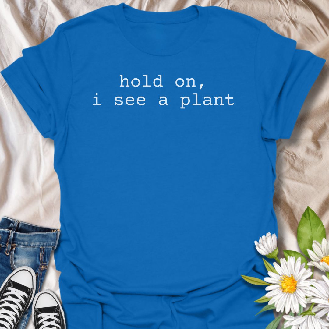A funny plant T-shirt for anyone who gets instantly distracted the moment a houseplant comes into view. The phrase “Hold On, I See a Plant” captures that familiar plant-lover behavior with simple, dry humor. Its clean typewriter-style text keeps the design minimal, modern, and very easy to wear. It makes a great gift for plant parents, houseplant collectors, nursery regulars, and anyone whose attention is permanently drawn to greenery. Perfect for plant shopping, garden centers, casual weekends, or everyday