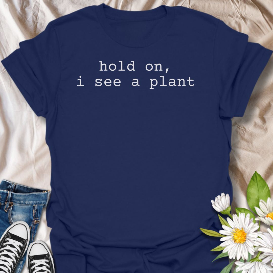 A funny plant T-shirt for anyone who gets instantly distracted the moment a houseplant comes into view. The phrase “Hold On, I See a Plant” captures that familiar plant-lover behavior with simple, dry humor. Its clean typewriter-style text keeps the design minimal, modern, and very easy to wear. It makes a great gift for plant parents, houseplant collectors, nursery regulars, and anyone whose attention is permanently drawn to greenery. Perfect for plant shopping, garden centers, casual weekends, or everyday