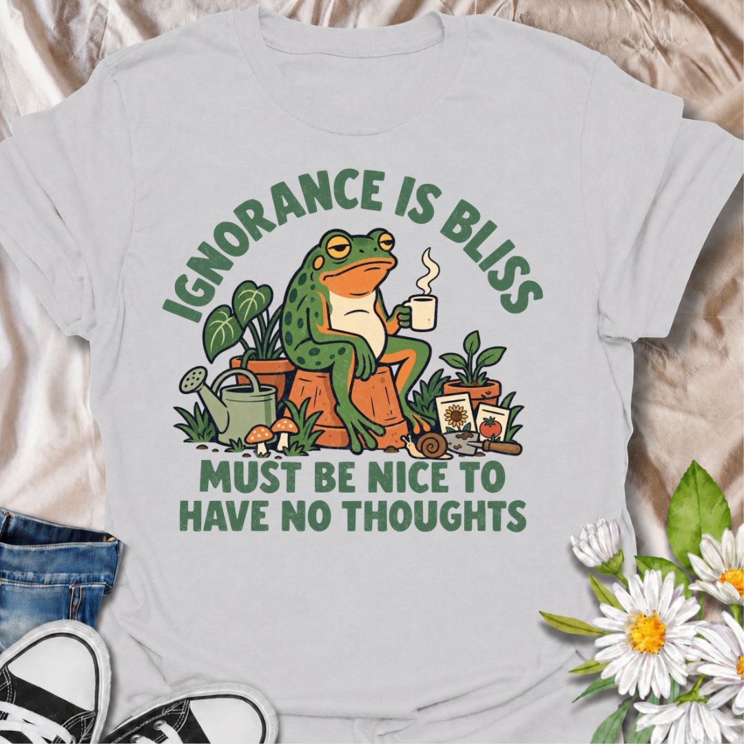A funny gardening T-shirt for anyone who suspects life might be easier with fewer thoughts and more time around plants. The phrase “Ignorance Is Bliss — Must Be Nice to Have No Thoughts” pairs with a deadpan frog, coffee mug, potted plants, and gardening supplies for sarcastic, character-led humor. It is perfect for gardeners, plant lovers, frog fans, and anyone who enjoys a slightly dry, absurd joke. The retro illustration gives the design plenty of personality while keeping it firmly rooted in the gardeni