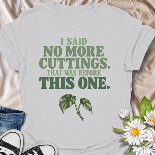 A funny propagation T-shirt for anyone who swore they were done taking cuttings until the next irresistible stem appeared. The phrase “I Said No More Cuttings. That Was Before This One.” captures the familiar logic of plant lovers who can always justify one more propagation. Featuring a simple leafy cutting beneath bold retro typography, the design stays clean, readable, and easy to wear. It makes a great gift for houseplant collectors, pothos lovers, propagation fans, and anyone with jars of cuttings takin