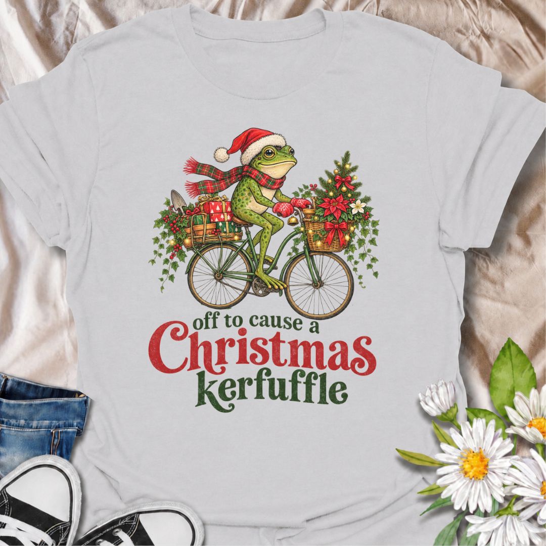 A funny Christmas gardening T-shirt featuring a determined frog cycling off to cause a little festive trouble. The phrase “Off to Cause a Christmas Kerfuffle” combines Botanic Weave’s deadpan frog humor with holly, gifts, garden tools, and plenty of Christmas cheer. It is perfect for gardeners, frog lovers, plant people, and anyone who prefers their holiday shirts funny rather than overly sweet. The detailed vintage-style illustration gives it a festive storybook feel while keeping the joke front and center