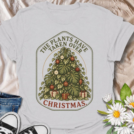 A festive houseplant T-shirt for anyone whose plants have officially taken over Christmas too. The phrase “The Plants Have Taken Over Christmas” surrounds a lush Christmas-tree-shaped mass of monstera and trailing foliage decorated with lights, ornaments, and gifts. It is perfect for plant parents, houseplant collectors, indoor gardeners, and anyone who would happily decorate their plants instead of a traditional tree. The detailed botanical artwork gives the design a rich vintage Christmas feel while still