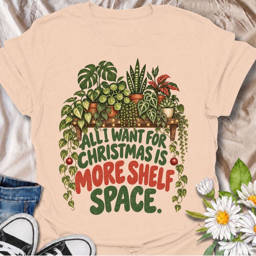 A funny Christmas plant T-shirt for anyone whose real holiday wish is simply more room for houseplants. The phrase “All I Want for Christmas Is More Shelf Space” pairs with a lush plant-filled shelf, trailing vines, fairy lights, and festive ornaments for a design made especially for serious plant collectors. It is perfect for plant parents, houseplant lovers, indoor gardeners, and anyone whose shelves are already overflowing with greenery. The Christmas details make it festive without losing the everyday p