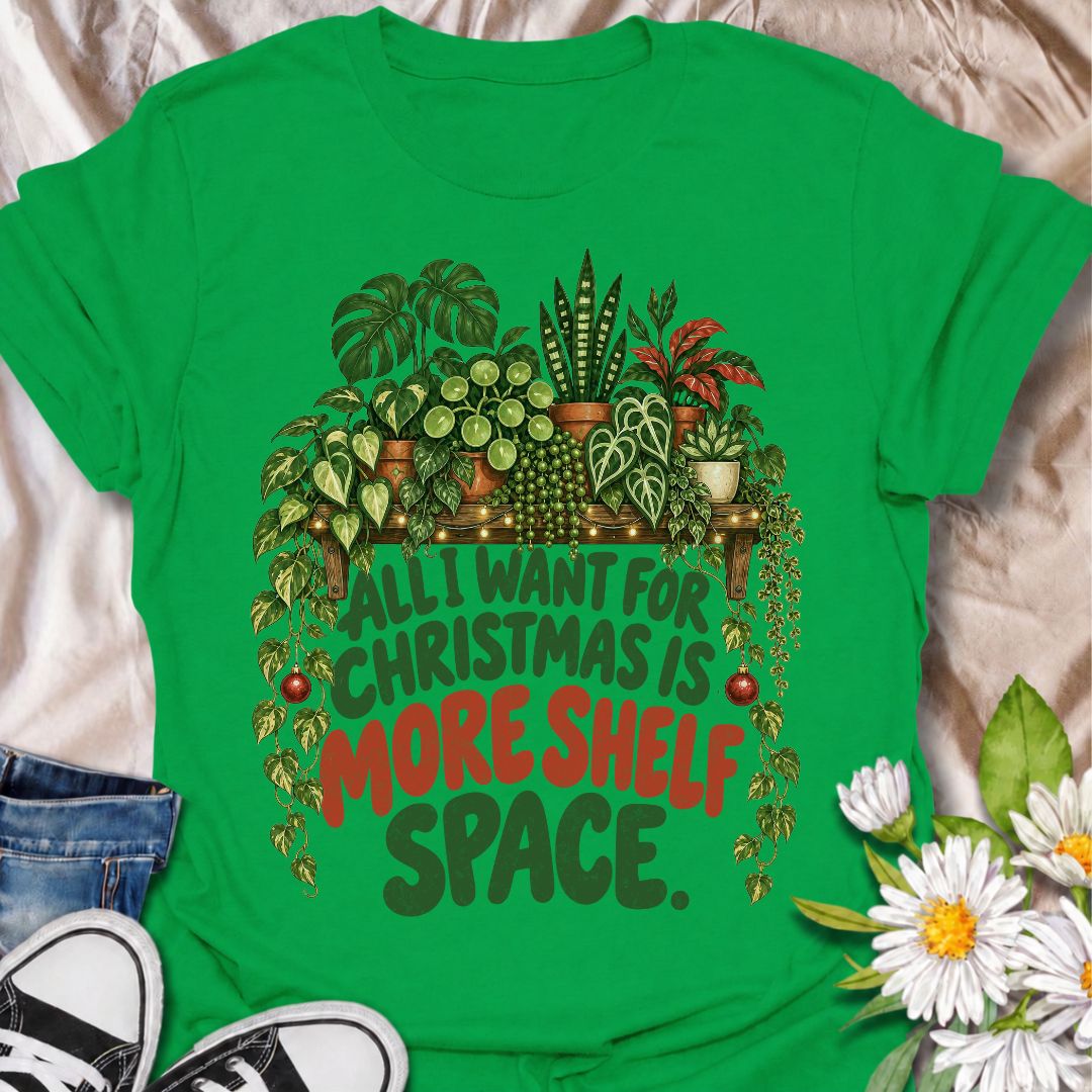 A funny Christmas plant T-shirt for anyone whose real holiday wish is simply more room for houseplants. The phrase “All I Want for Christmas Is More Shelf Space” pairs with a lush plant-filled shelf, trailing vines, fairy lights, and festive ornaments for a design made especially for serious plant collectors. It is perfect for plant parents, houseplant lovers, indoor gardeners, and anyone whose shelves are already overflowing with greenery. The Christmas details make it festive without losing the everyday p