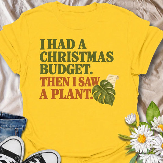 A funny Christmas plant T-shirt for anyone whose festive budget disappeared the moment another houseplant came into view. The phrase “I Had a Christmas Budget. Then I Saw a Plant.” delivers dry, relatable humor for plant parents, nursery regulars, and houseplant collectors. Featuring bold retro typography with a monstera leaf and receipt detail, the design stays clean, festive, and easy to wear. It makes a great Christmas gift for plant lovers who know seasonal spending rarely survives a trip to the garden 