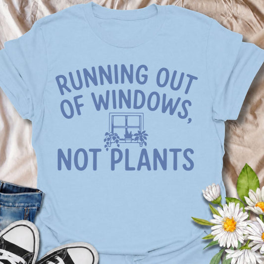 A funny houseplant T-shirt for anyone who is running out of sunny windows long before they are running out of plants. The phrase “Running Out of Windows, Not Plants” captures the reality of an ever-growing indoor jungle with simple, relatable humor. Featuring a small windowsill filled with potted plants, the design is perfect for plant parents, houseplant collectors, and indoor gardeners. It makes a great gift for anyone whose best light has already been claimed by greenery. Perfect for nursery trips, plant