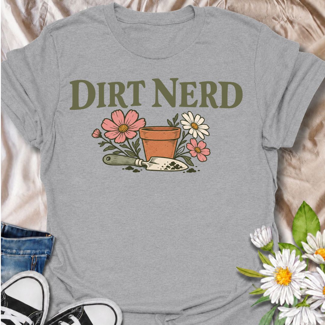 A playful gardening T-shirt for anyone who genuinely gets excited about soil, pots, planting, and everything that goes with growing things. The simple “Dirt Nerd” phrase pairs with flowers, a terracotta pot, and hand trowel for a clean garden-lover design with plenty of personality. It is perfect for backyard gardeners, flower growers, cottage gardeners, and anyone who is happiest with their hands in the soil. The soft vintage-style artwork keeps the design cheerful and easy to wear. A great gift for garden