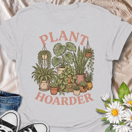 A fun houseplant T-shirt for anyone whose plant collection has clearly moved beyond “a few favorites.” The bold “Plant Hoarder” phrase is surrounded by monstera, snake plants, ferns, trailing vines, and succulents for a lush botanical design made for serious plant lovers. It is perfect for plant parents, indoor gardeners, nursery regulars, and anyone whose home is steadily turning into an indoor jungle. The vintage-inspired artwork gives the design a softer, decorative feel while keeping the message easy to