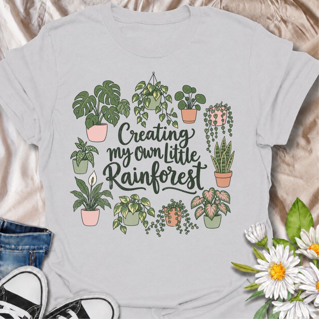 A charming houseplant T-shirt for anyone who is slowly turning their home into a lush indoor jungle. The phrase “Creating My Own Little Rainforest” is surrounded by monstera, pothos, snake plants, trailing vines, and other leafy favorites for a soft botanical design. It is perfect for plant parents, houseplant collectors, indoor gardeners, and anyone who loves filling every spare corner with greenery. The hand-drawn styling gives it a warm, feminine feel while keeping the design easy to wear. A lovely gift 