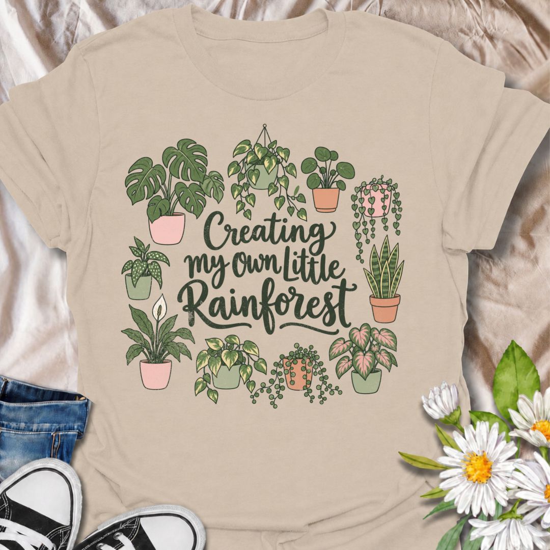 A charming houseplant T-shirt for anyone who is slowly turning their home into a lush indoor jungle. The phrase “Creating My Own Little Rainforest” is surrounded by monstera, pothos, snake plants, trailing vines, and other leafy favorites for a soft botanical design. It is perfect for plant parents, houseplant collectors, indoor gardeners, and anyone who loves filling every spare corner with greenery. The hand-drawn styling gives it a warm, feminine feel while keeping the design easy to wear. A lovely gift 