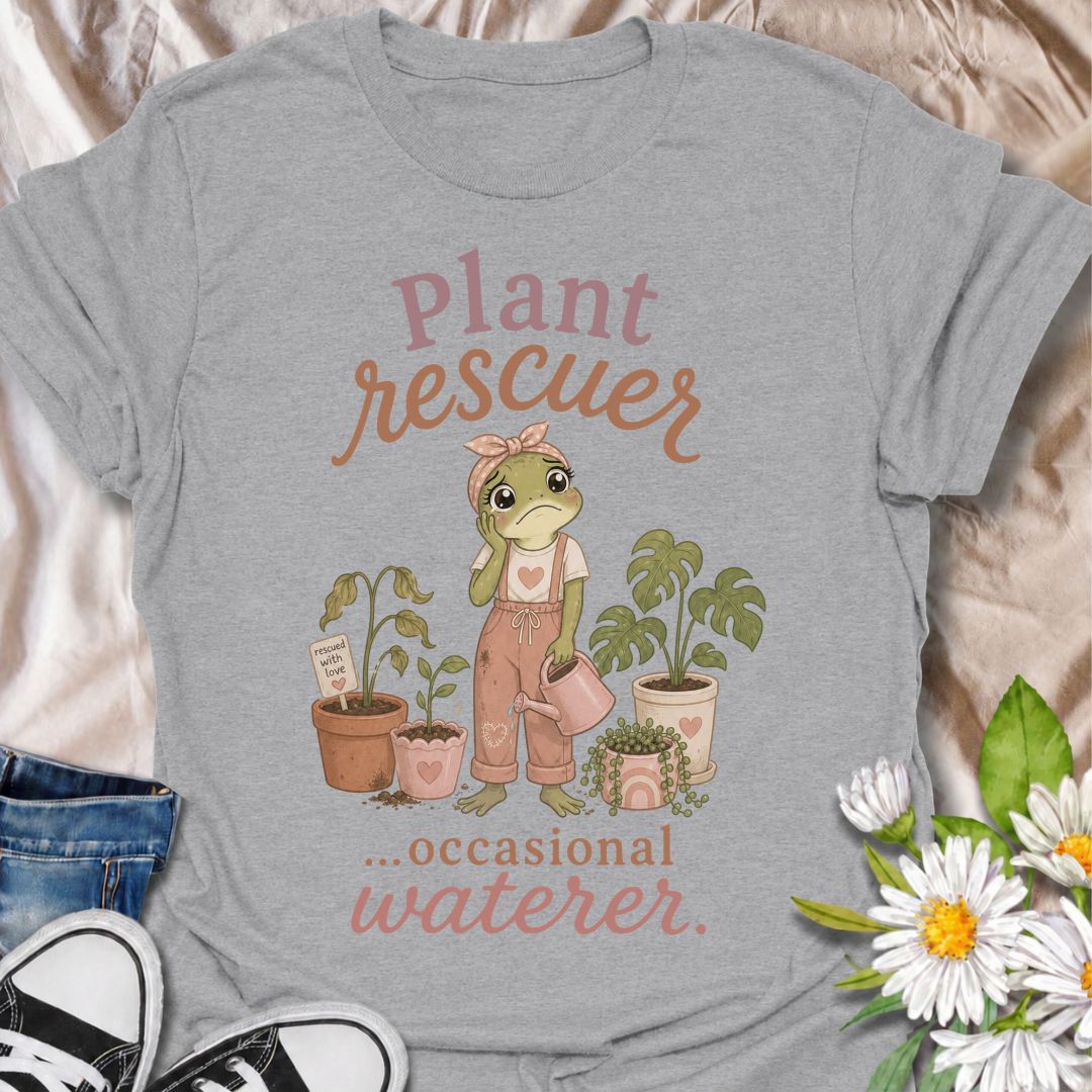 A funny plant T-shirt for anyone who cannot resist trying to save a struggling houseplant. The phrase “Plant Rescuer… Occasional Waterer” pairs with a sweet frog character, wilted plants, watering can, and potted greenery for playful, self-aware plant-parent humor. It is perfect for houseplant lovers, indoor gardeners, and anyone who brings home sad plants with every intention of nursing them back to health. The softer pastel artwork gives the design a warm, feminine feel while keeping the joke clear and re