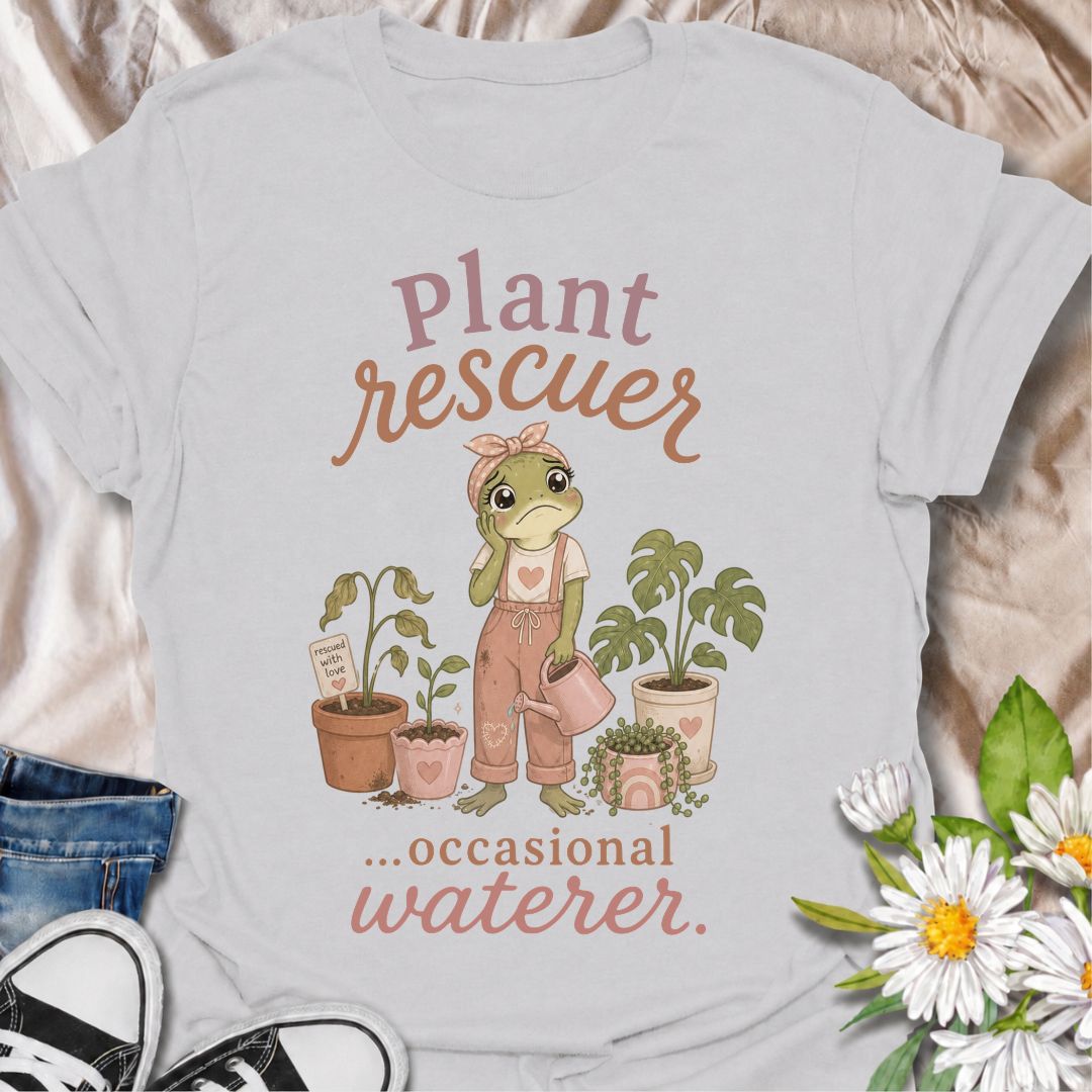 A funny plant T-shirt for anyone who cannot resist trying to save a struggling houseplant. The phrase “Plant Rescuer… Occasional Waterer” pairs with a sweet frog character, wilted plants, watering can, and potted greenery for playful, self-aware plant-parent humor. It is perfect for houseplant lovers, indoor gardeners, and anyone who brings home sad plants with every intention of nursing them back to health. The softer pastel artwork gives the design a warm, feminine feel while keeping the joke clear and re