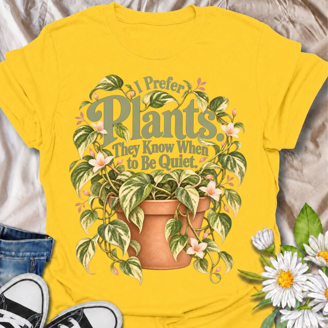 A charming plant T-shirt for anyone who prefers the company of houseplants and appreciates a little peace and quiet. The phrase “I Prefer Plants. They Know When to Be Quiet.” pairs with a lush variegated trailing plant, soft pink flowers, and a terracotta pot for gentle, relatable plant-lover humor. It is perfect for plant parents, houseplant collectors, indoor gardeners, and anyone who enjoys calm spaces filled with greenery. The muted sage, cream, blush, and terracotta palette gives the design a softer, m