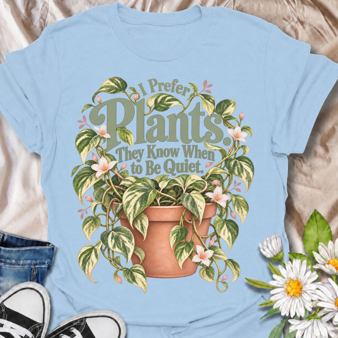 A charming plant T-shirt for anyone who prefers the company of houseplants and appreciates a little peace and quiet. The phrase “I Prefer Plants. They Know When to Be Quiet.” pairs with a lush variegated trailing plant, soft pink flowers, and a terracotta pot for gentle, relatable plant-lover humor. It is perfect for plant parents, houseplant collectors, indoor gardeners, and anyone who enjoys calm spaces filled with greenery. The muted sage, cream, blush, and terracotta palette gives the design a softer, m