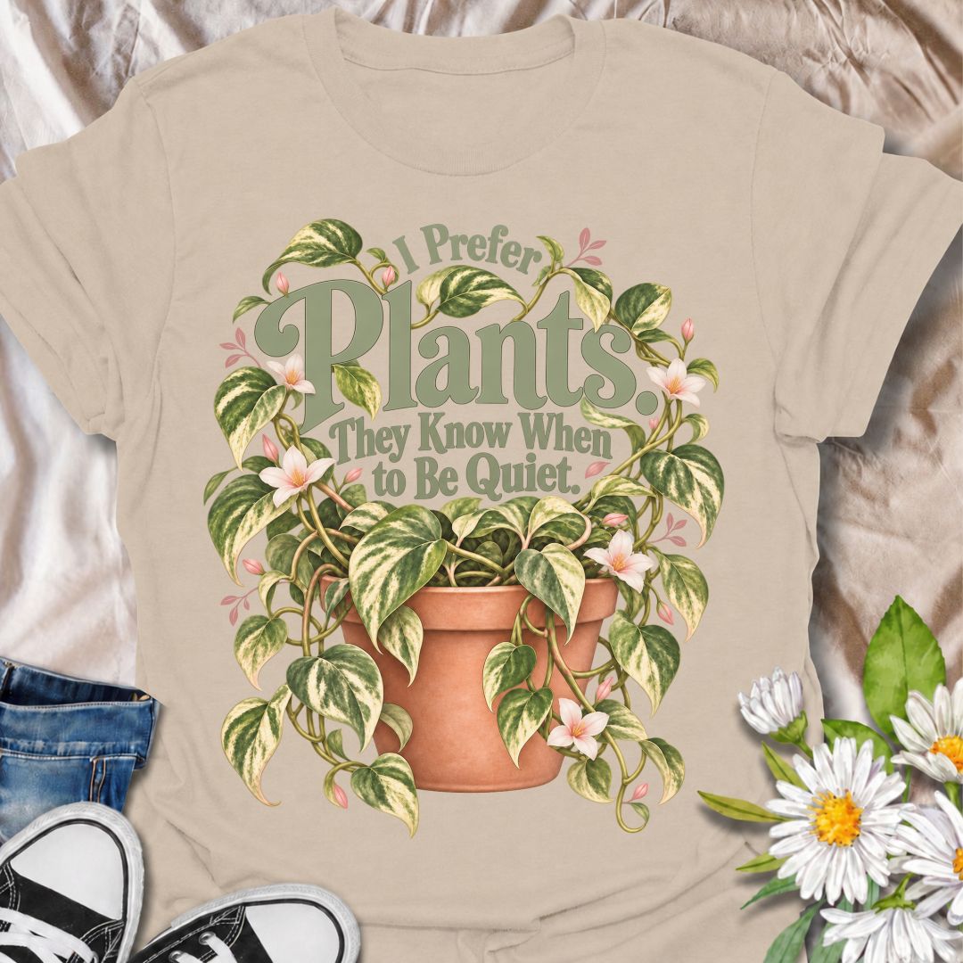 A charming plant T-shirt for anyone who prefers the company of houseplants and appreciates a little peace and quiet. The phrase “I Prefer Plants. They Know When to Be Quiet.” pairs with a lush variegated trailing plant, soft pink flowers, and a terracotta pot for gentle, relatable plant-lover humor. It is perfect for plant parents, houseplant collectors, indoor gardeners, and anyone who enjoys calm spaces filled with greenery. The muted sage, cream, blush, and terracotta palette gives the design a softer, m