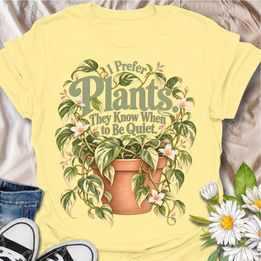 A charming plant T-shirt for anyone who prefers the company of houseplants and appreciates a little peace and quiet. The phrase “I Prefer Plants. They Know When to Be Quiet.” pairs with a lush variegated trailing plant, soft pink flowers, and a terracotta pot for gentle, relatable plant-lover humor. It is perfect for plant parents, houseplant collectors, indoor gardeners, and anyone who enjoys calm spaces filled with greenery. The muted sage, cream, blush, and terracotta palette gives the design a softer, m