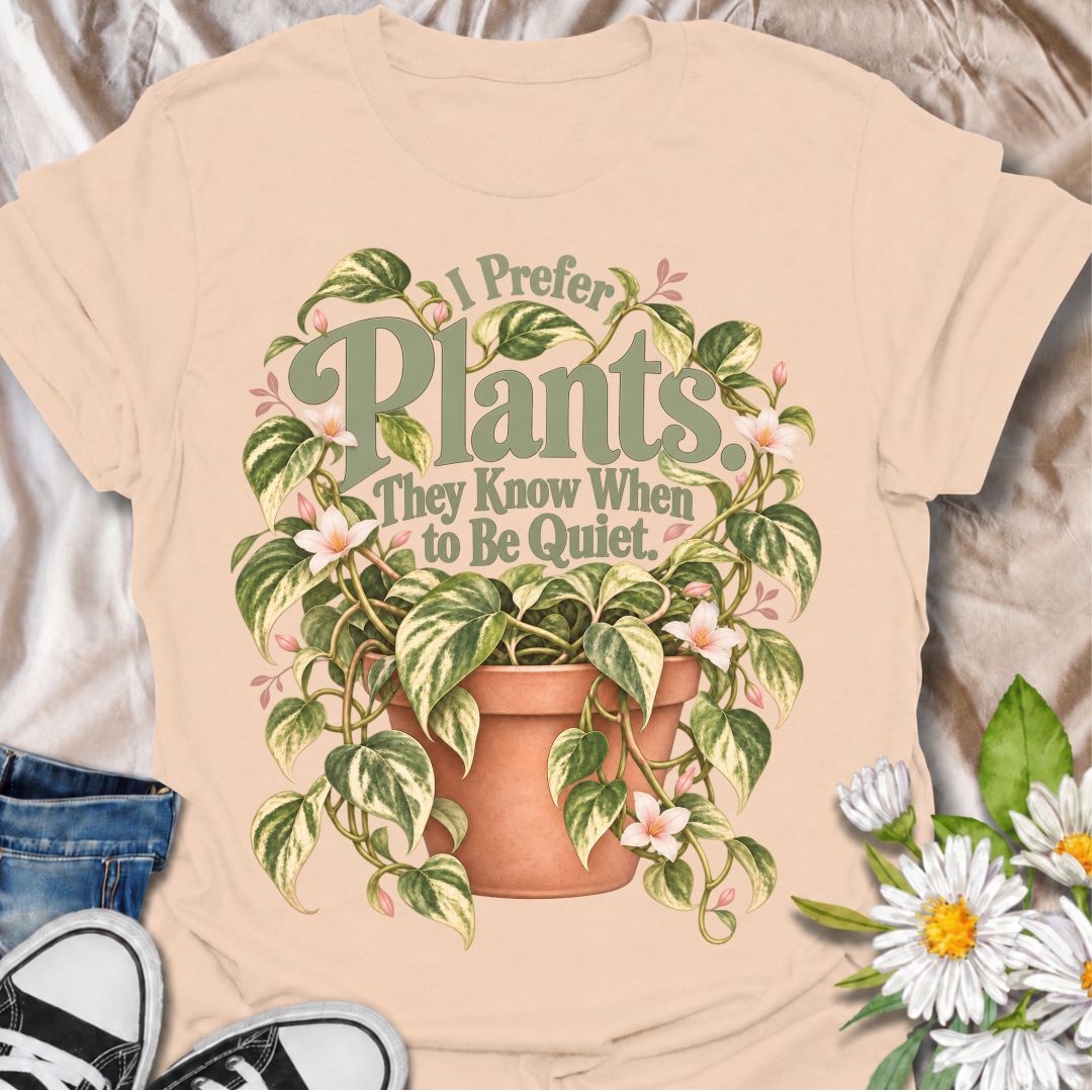 A charming plant T-shirt for anyone who prefers the company of houseplants and appreciates a little peace and quiet. The phrase “I Prefer Plants. They Know When to Be Quiet.” pairs with a lush variegated trailing plant, soft pink flowers, and a terracotta pot for gentle, relatable plant-lover humor. It is perfect for plant parents, houseplant collectors, indoor gardeners, and anyone who enjoys calm spaces filled with greenery. The muted sage, cream, blush, and terracotta palette gives the design a softer, m