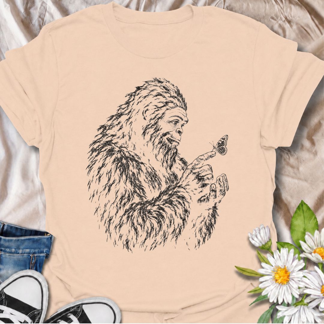 A gentle Bigfoot T-shirt for nature lovers who appreciate the quieter side of the wilderness. Featuring a hand-drawn Bigfoot carefully watching a butterfly resting on his fingertip, this design combines woodland folklore with a soft, unexpected moment of curiosity. It is perfect for Bigfoot fans, gardeners, pollinator lovers, hikers, and anyone drawn to whimsical nature-inspired artwork. The monochrome sketch style gives the design a vintage field-guide feel without becoming overly busy. A distinctive gift 