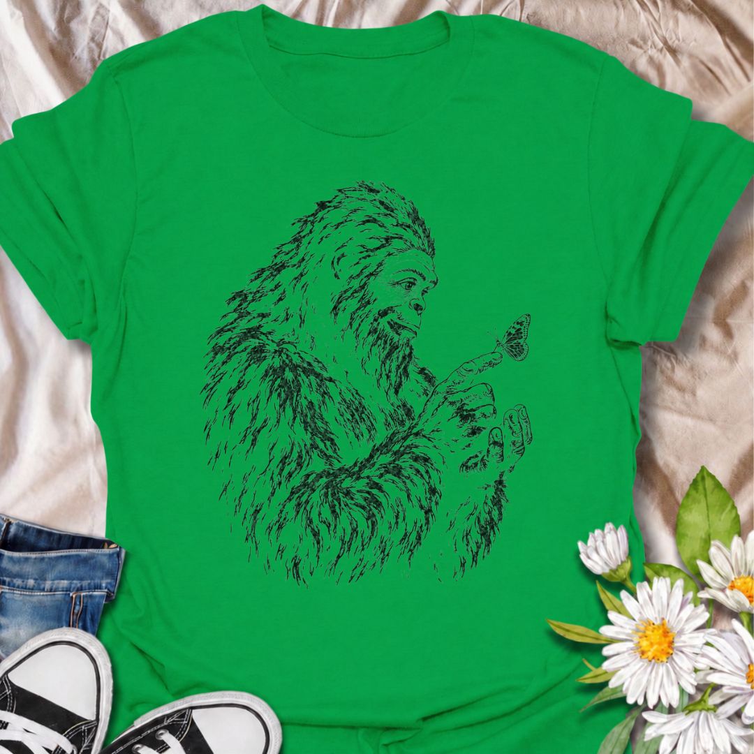 A gentle Bigfoot T-shirt for nature lovers who appreciate the quieter side of the wilderness. Featuring a hand-drawn Bigfoot carefully watching a butterfly resting on his fingertip, this design combines woodland folklore with a soft, unexpected moment of curiosity. It is perfect for Bigfoot fans, gardeners, pollinator lovers, hikers, and anyone drawn to whimsical nature-inspired artwork. The monochrome sketch style gives the design a vintage field-guide feel without becoming overly busy. A distinctive gift 