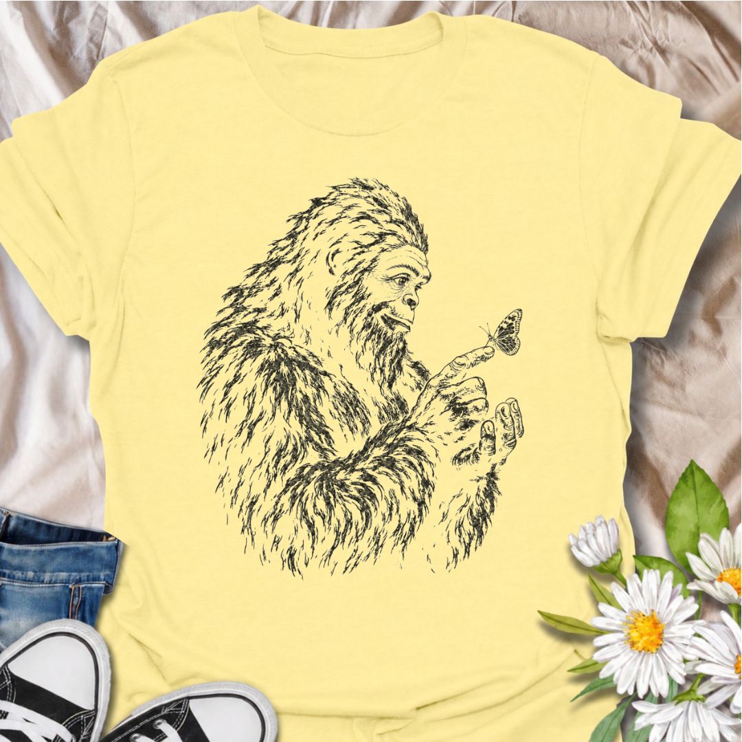 A gentle Bigfoot T-shirt for nature lovers who appreciate the quieter side of the wilderness. Featuring a hand-drawn Bigfoot carefully watching a butterfly resting on his fingertip, this design combines woodland folklore with a soft, unexpected moment of curiosity. It is perfect for Bigfoot fans, gardeners, pollinator lovers, hikers, and anyone drawn to whimsical nature-inspired artwork. The monochrome sketch style gives the design a vintage field-guide feel without becoming overly busy. A distinctive gift 