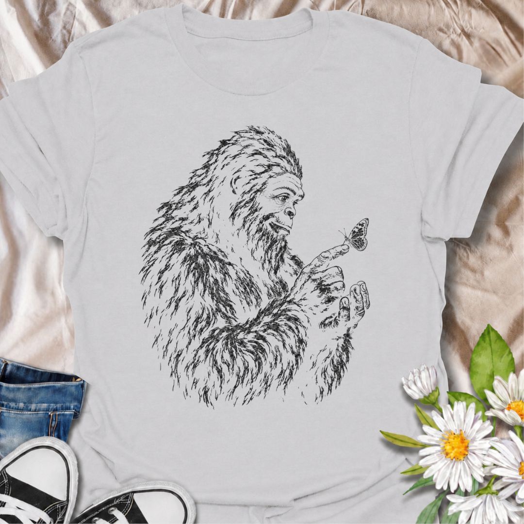 A gentle Bigfoot T-shirt for nature lovers who appreciate the quieter side of the wilderness. Featuring a hand-drawn Bigfoot carefully watching a butterfly resting on his fingertip, this design combines woodland folklore with a soft, unexpected moment of curiosity. It is perfect for Bigfoot fans, gardeners, pollinator lovers, hikers, and anyone drawn to whimsical nature-inspired artwork. The monochrome sketch style gives the design a vintage field-guide feel without becoming overly busy. A distinctive gift 