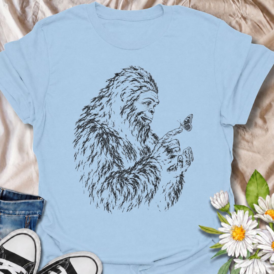 A gentle Bigfoot T-shirt for nature lovers who appreciate the quieter side of the wilderness. Featuring a hand-drawn Bigfoot carefully watching a butterfly resting on his fingertip, this design combines woodland folklore with a soft, unexpected moment of curiosity. It is perfect for Bigfoot fans, gardeners, pollinator lovers, hikers, and anyone drawn to whimsical nature-inspired artwork. The monochrome sketch style gives the design a vintage field-guide feel without becoming overly busy. A distinctive gift 