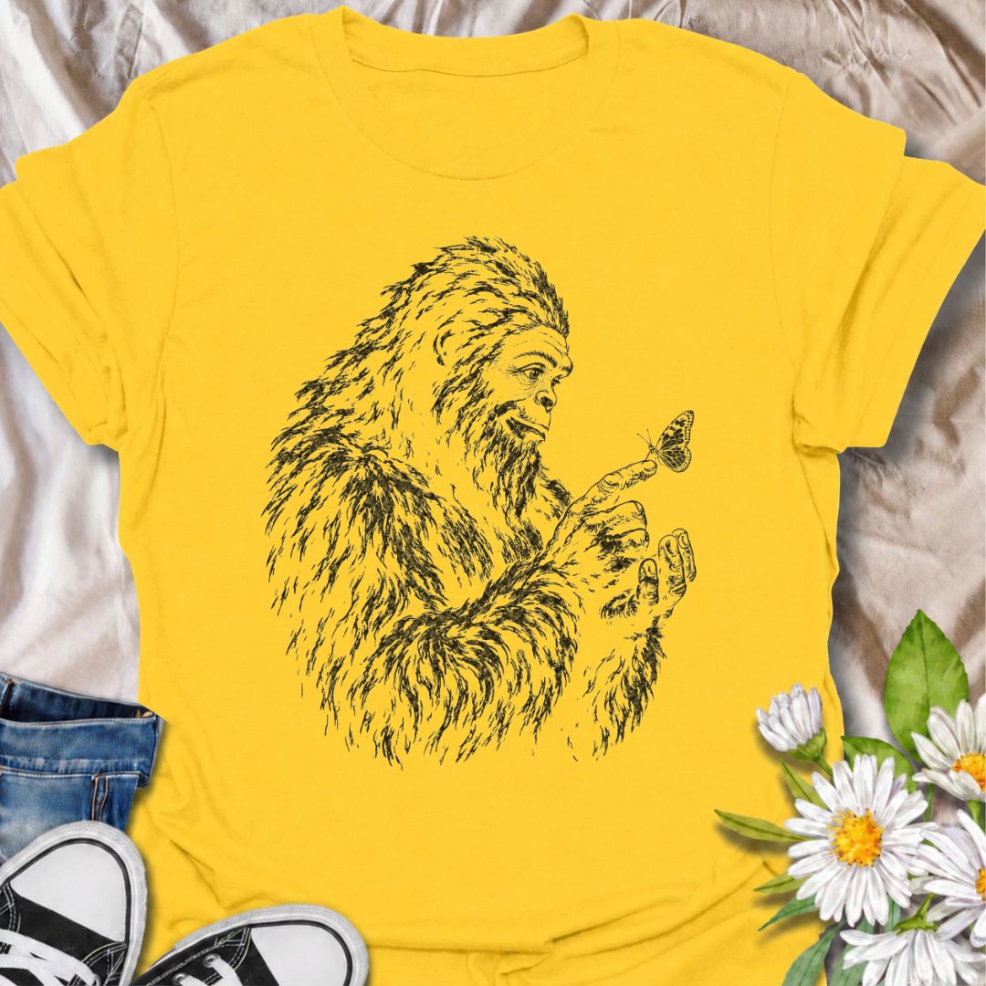 A gentle Bigfoot T-shirt for nature lovers who appreciate the quieter side of the wilderness. Featuring a hand-drawn Bigfoot carefully watching a butterfly resting on his fingertip, this design combines woodland folklore with a soft, unexpected moment of curiosity. It is perfect for Bigfoot fans, gardeners, pollinator lovers, hikers, and anyone drawn to whimsical nature-inspired artwork. The monochrome sketch style gives the design a vintage field-guide feel without becoming overly busy. A distinctive gift 