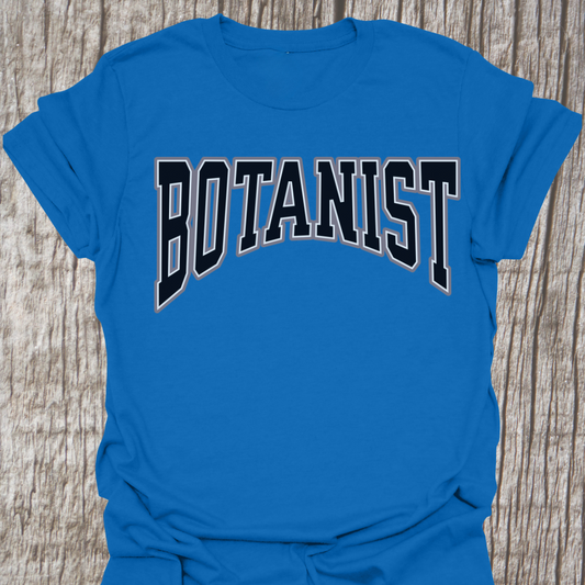 Black text with a small white border stating "botanist", text is in a small arc.  Botanist is printed onto a royal blue t-shirt