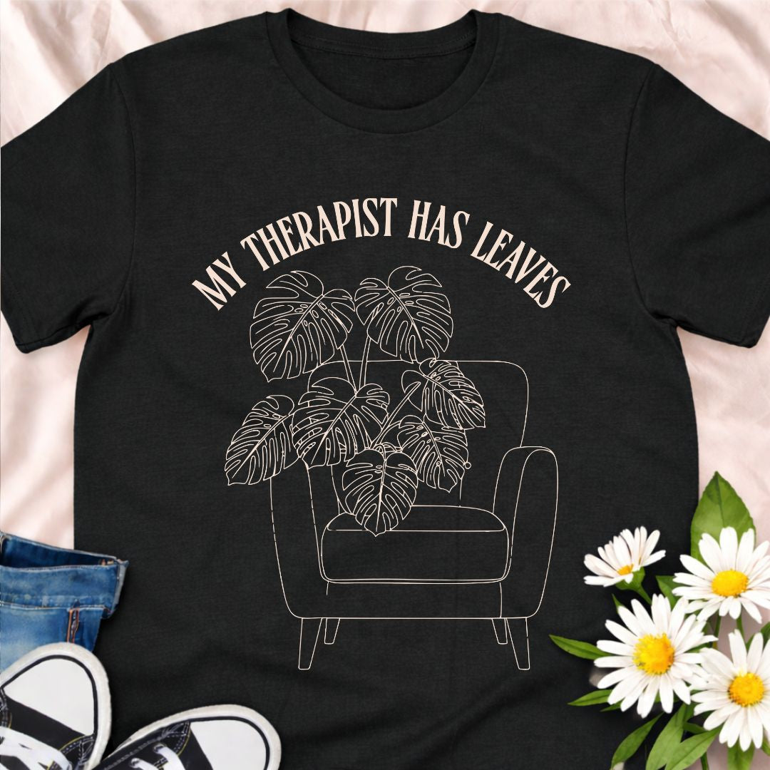 For plant people who spill their heart out to their houseplants, this “My Therapist Has Leaves” t-shirt says it all. Features a cozy armchair and lush monstera, making it the perfect aesthetic plant lover tee for self-care days.