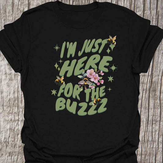 I am Just Here For The Buzz Black T-shirt, featuring a green text design adorned with bees and flowers for decoration