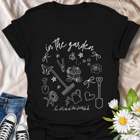 Charming "In The Garden" doodle style t-shirt with hand-drawn gardening tools, flowers, and butterflies. Perfect gift for gardeners, plant lovers, and nature enthusiasts. Stylish botanical apparel for spring, summer, or everyday wear. Celebrate your green thumb!