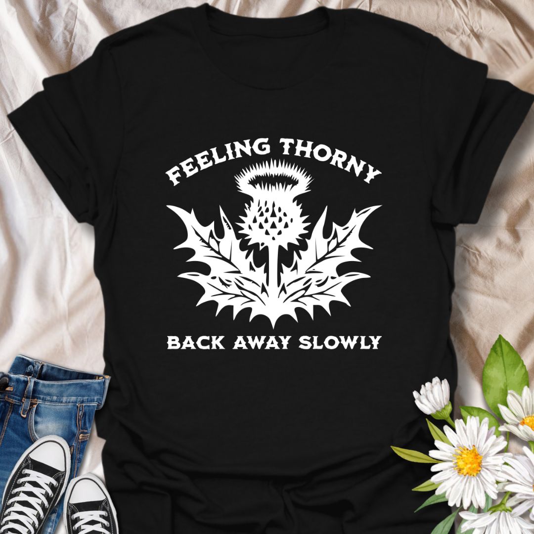 Embrace your mood with this witty “Feeling Thorny – Back Away Slowly” t-shirt featuring a bold thistle graphic. Perfect for introverts, plant lovers, and anyone with a sharp sense of humor, this quirky design makes a great gift or statement piece for everyday wear.
