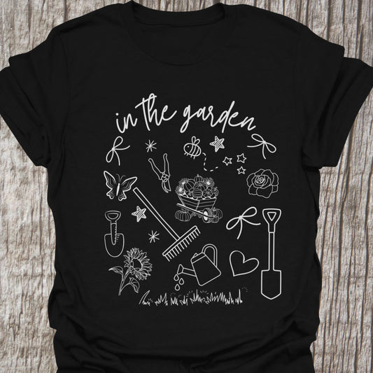 Garden Doodle on a T-shirt!  This doodle has garden tools, flowers, grass, bees, butterfly and lots more, white images and text saying 'in the garden'  on a black t-shirt