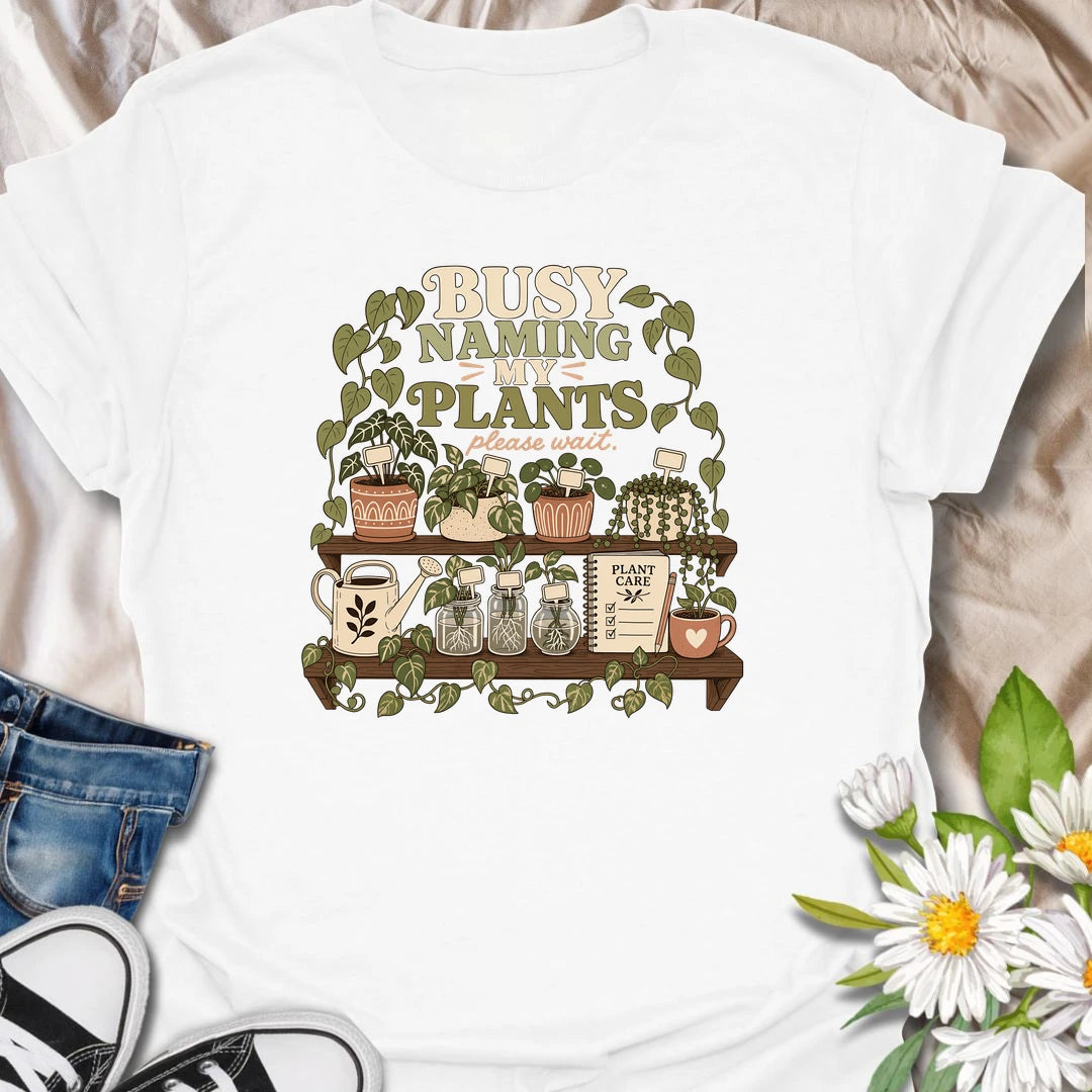 A funny plant lover T-shirt for anyone who treats every houseplant like part of the family. The detailed design features potted plants, propagation jars, gardening tools, and a plant care notebook. A charming gift for plant moms, houseplant collectors, and indoor gardening enthusiasts.