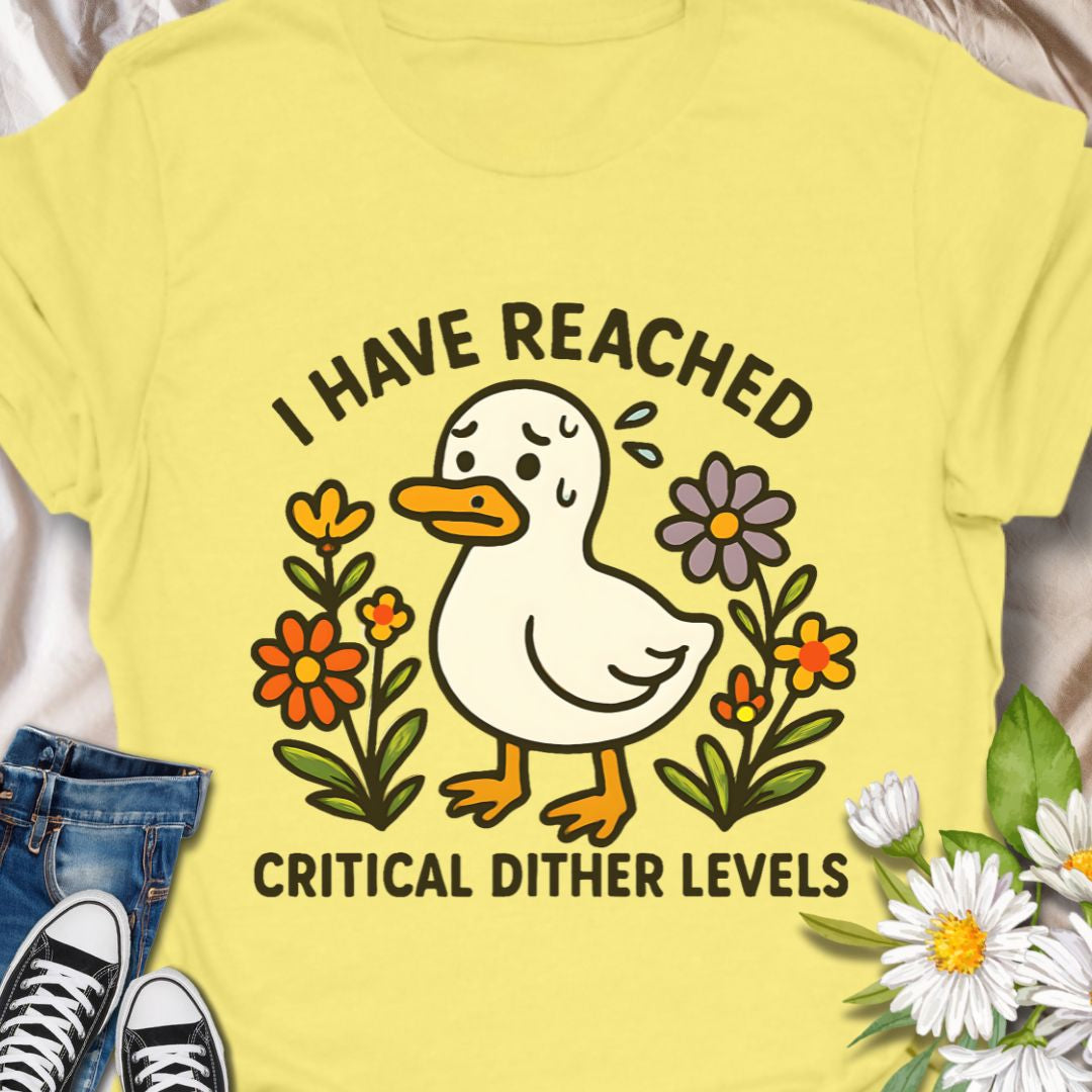 Soft, light, and quietly silly — this tee carries a tiny moment of honest feeling. A cheerful duck illustration stands among simple hand-drawn flowers with the line “I have reached critical dither levels.” Wear it when your brain is doing cartwheels and you need an outfit that says, with humor and a little compassion, “I’m wobbling but still okay.”